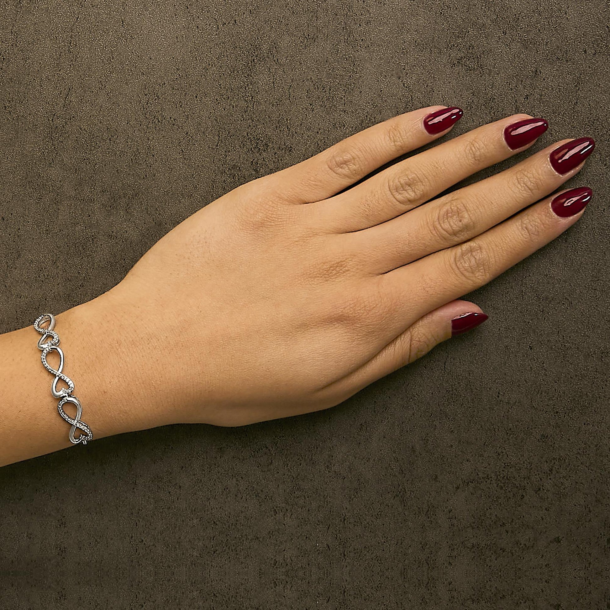 White metal bracelet with open heart and round white gemstones in prong settings, shown worn on a model's wrist, image taken from above.