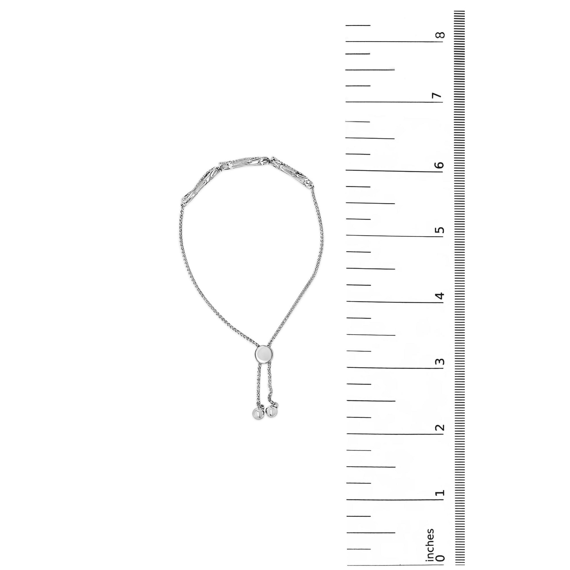 White bracelet with a central circular slider and adjustable ends, shown flat on a white background next to a scale, photographed from the top.