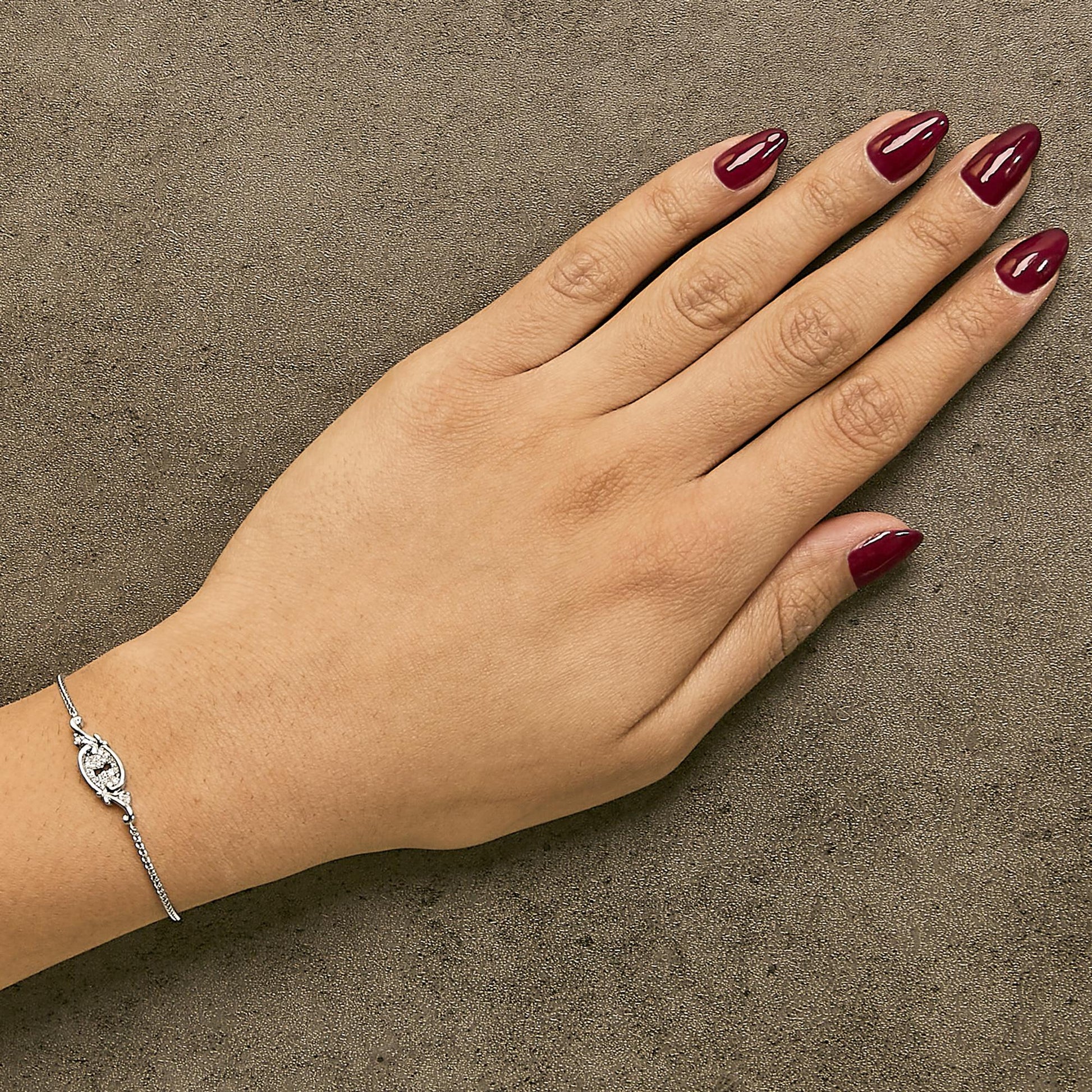 White metal bracelet with round white gemstones in a shared prong setting, shown worn on a model's wrist from a top angle.