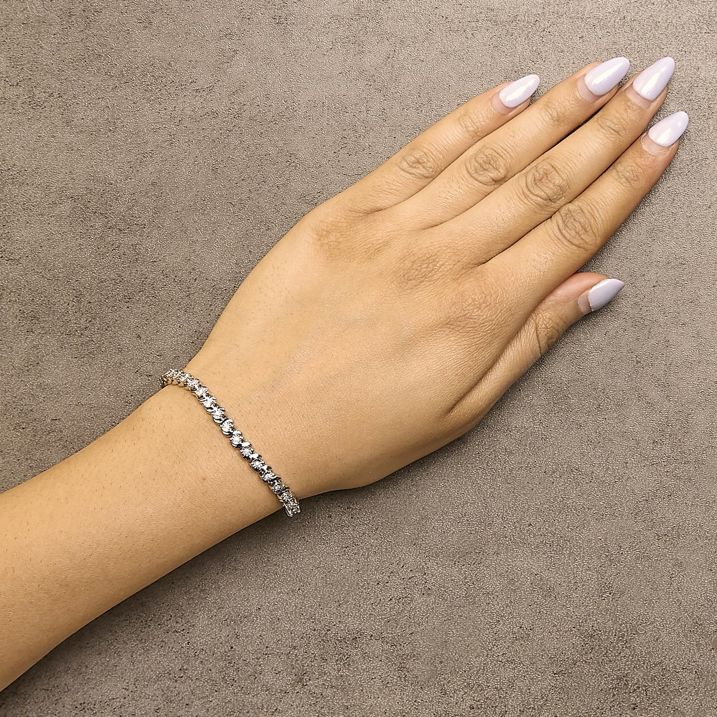 White metal bracelet with round white gemstones in miracle setting, shown worn on a model's wrist from a top angle.