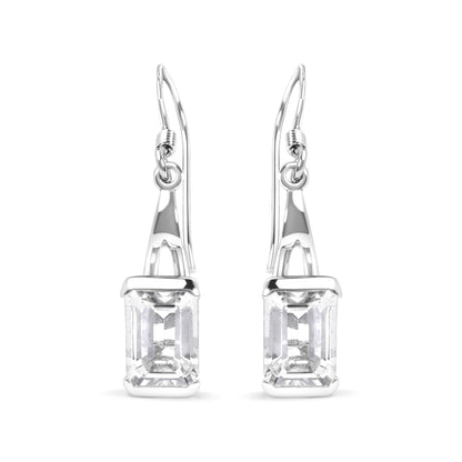 Front-facing image of white metal earrings with emerald-cut white gemstones in four-prong settings hanging from hooks.