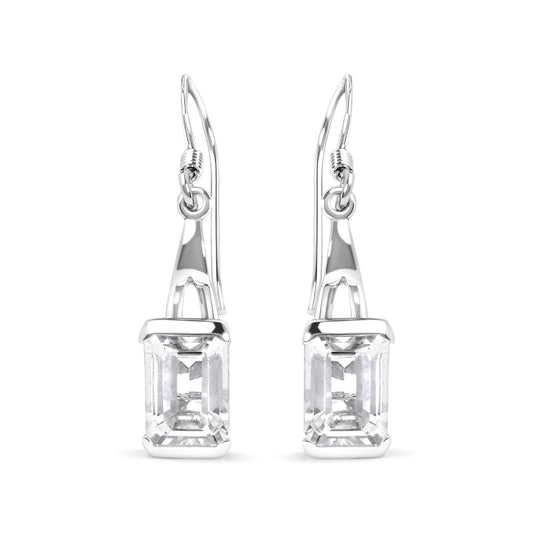 Front-facing image of white metal earrings with emerald-cut white gemstones in four-prong settings hanging from hooks.