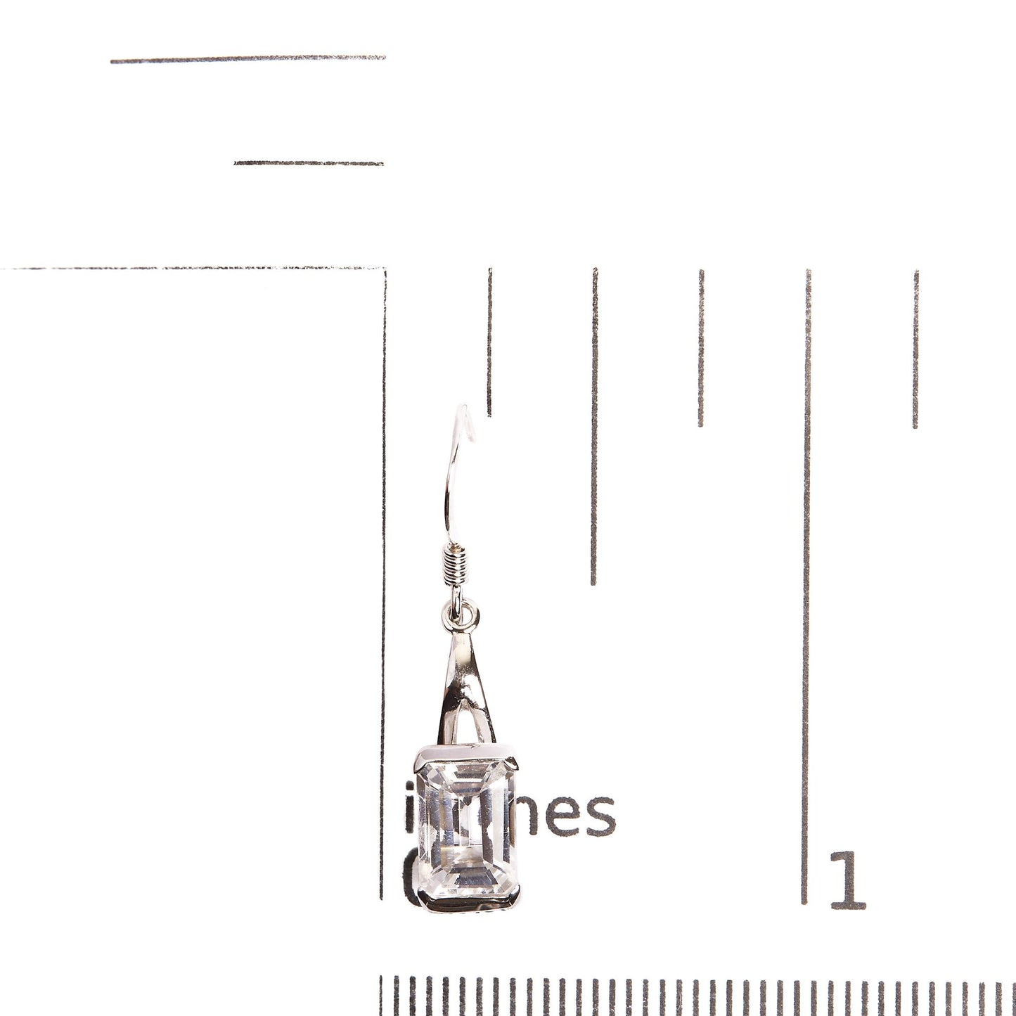Single white metal earring with a white, emerald-shaped gemstone in a four-prong setting, photographed on a ruler from a front angle.