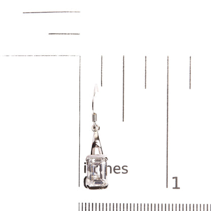 Single white metal earring with a white, emerald-shaped gemstone in a four-prong setting, photographed on a ruler from a front angle.