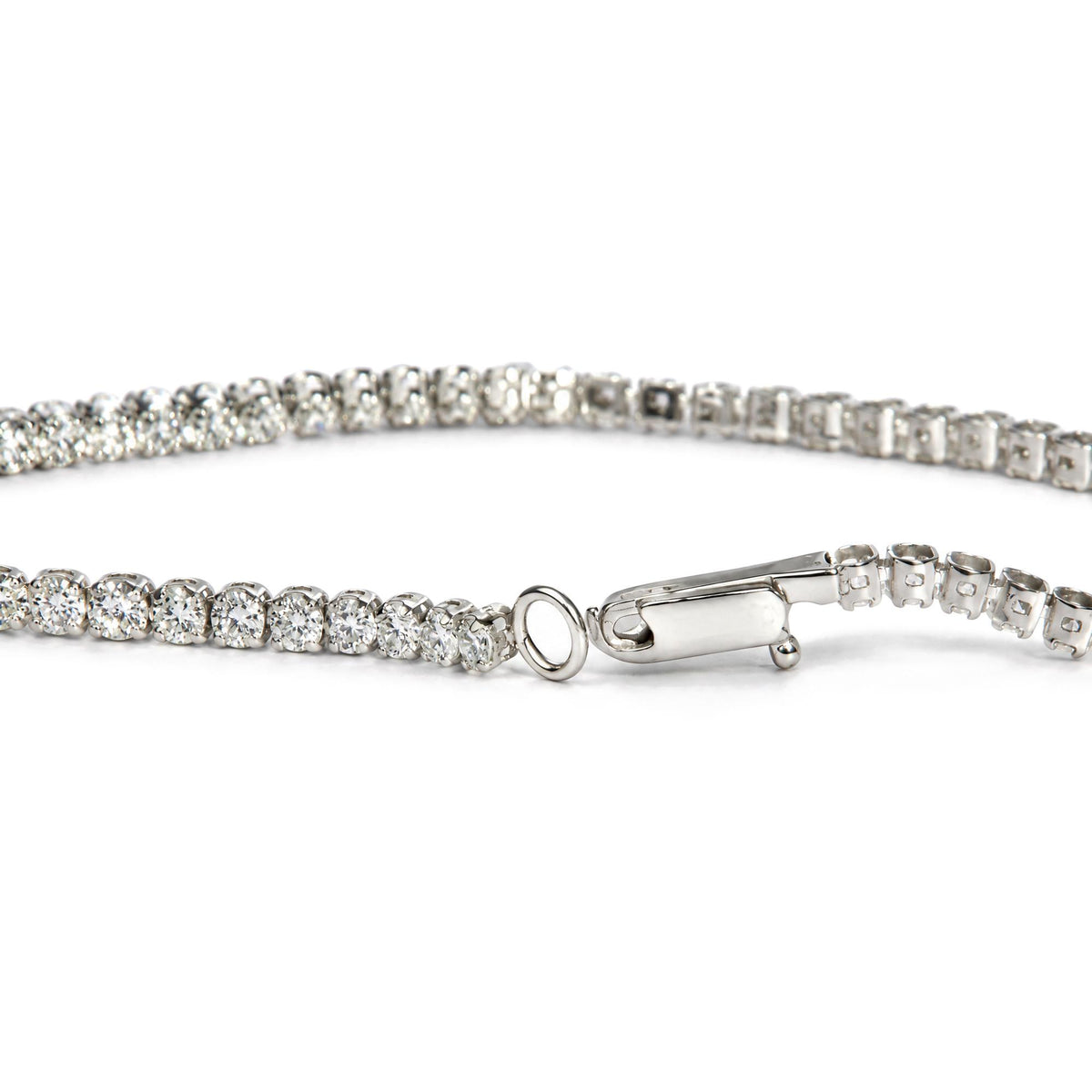 Close-up front angle of a white metal tennis bracelet featuring round white gemstones in prong settings, with the clasp and loop visible.