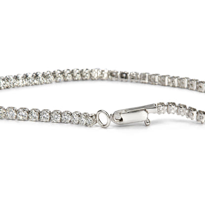 Close-up front angle of a white metal tennis bracelet featuring round white gemstones in prong settings, with the clasp and loop visible.
