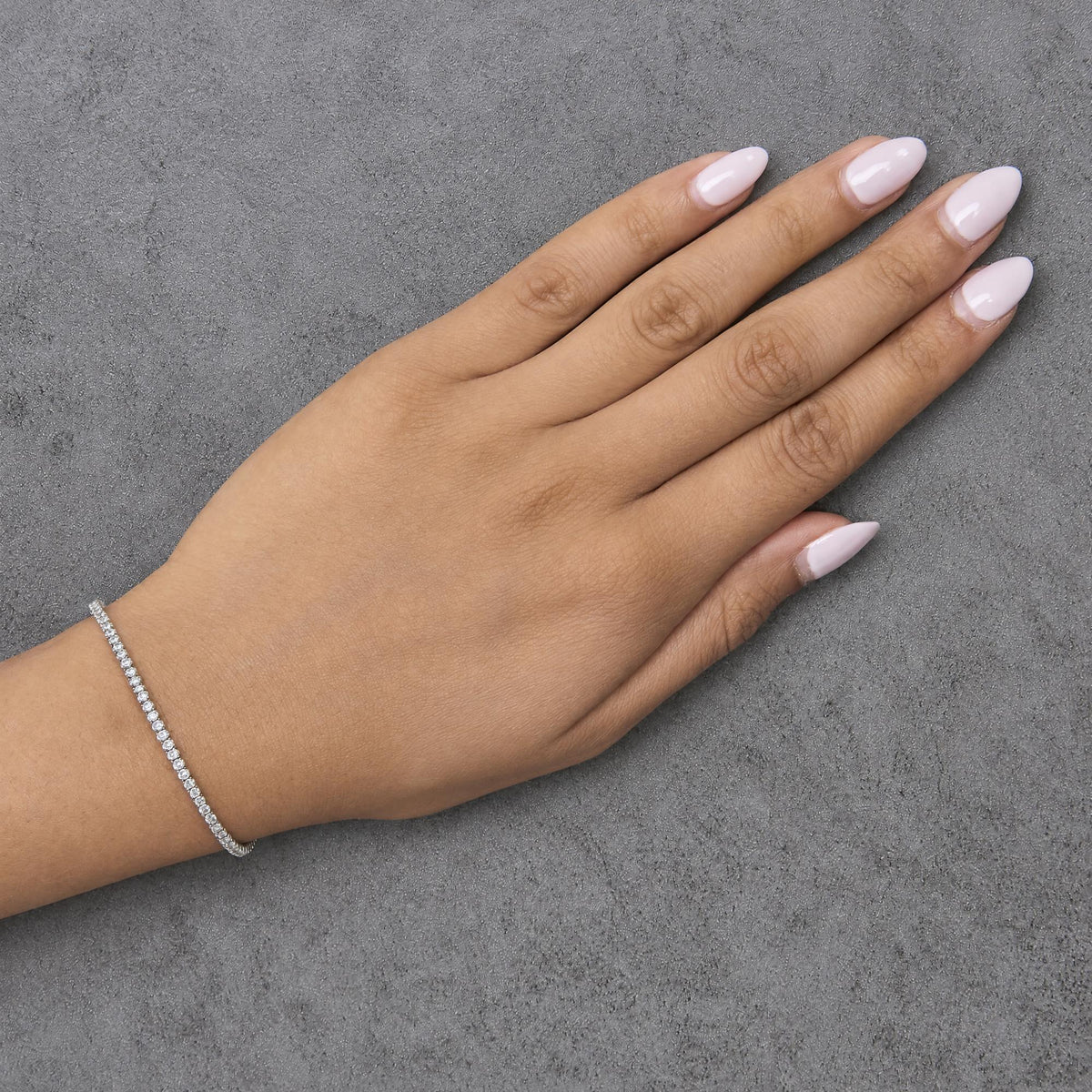 White metal bracelet with round white gemstones in prong setting, worn on model's wrist, angled top-down view.