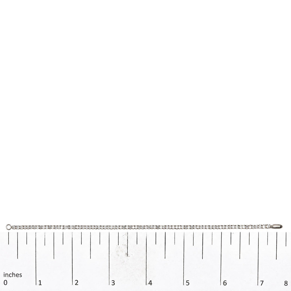 White metal bracelet with prong-set round white gemstones, displayed straight on a measuring scale, top-down view.