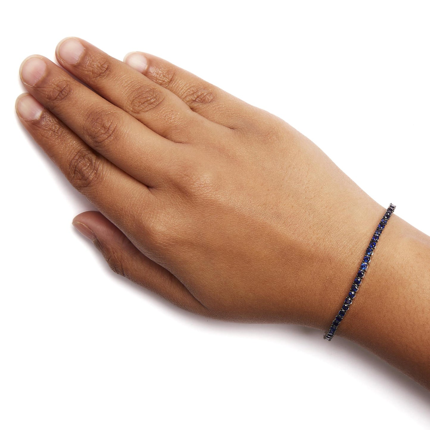 White metal bracelet with a row of round blue gemstones in shared prong setting, worn on a model's wrist, shot from above.