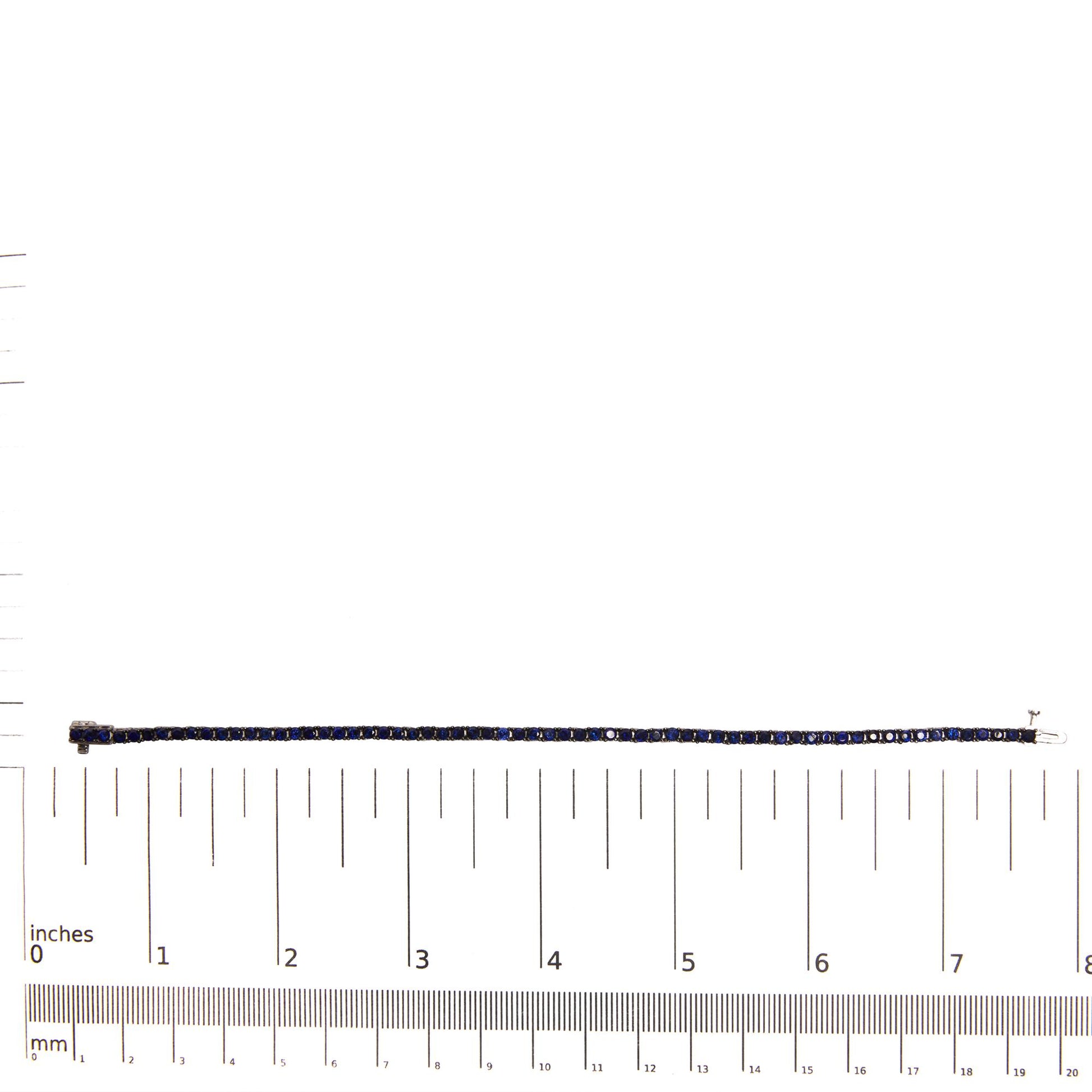 White metal bracelet with blue round gemstones in shared prong setting, laid flat on a ruler for size reference, top-down view.