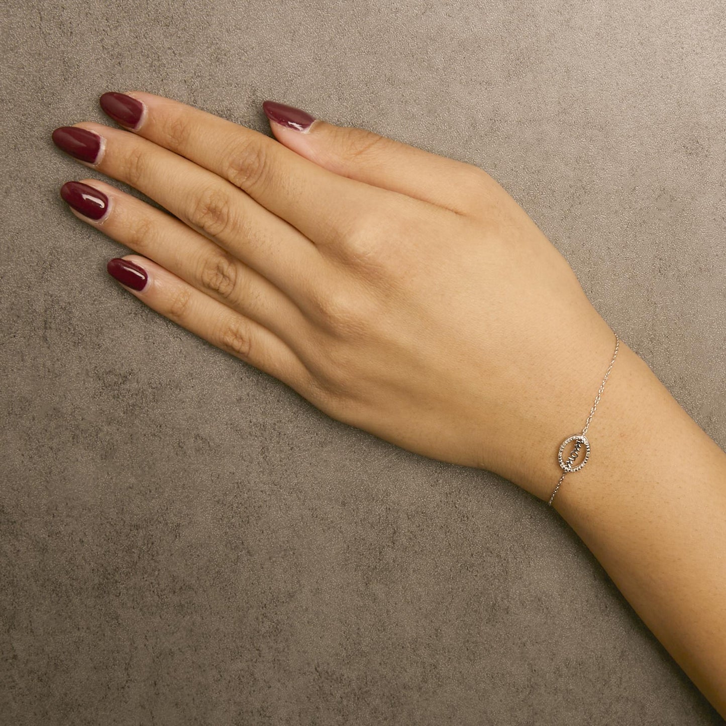 White metal bracelet with an oval centerpiece set with round white gemstones, worn on a model's wrist, shot from above.