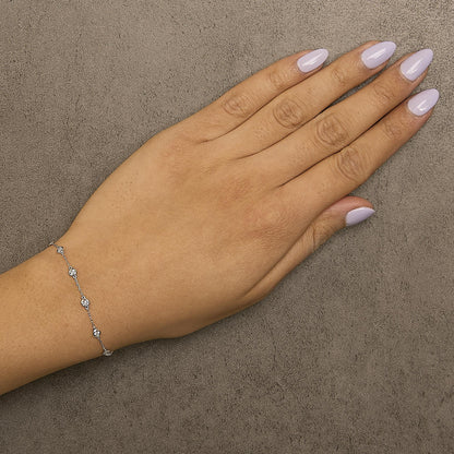 White metal bracelet with round bezel-set white gemstones, shown worn on a model's wrist from a top-down angle.