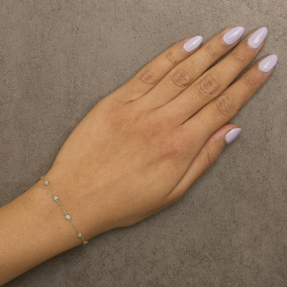 Close-up front view of a model's hand wearing a delicate yellow bracelet with round white gemstones in bezel settings along a thin chain.