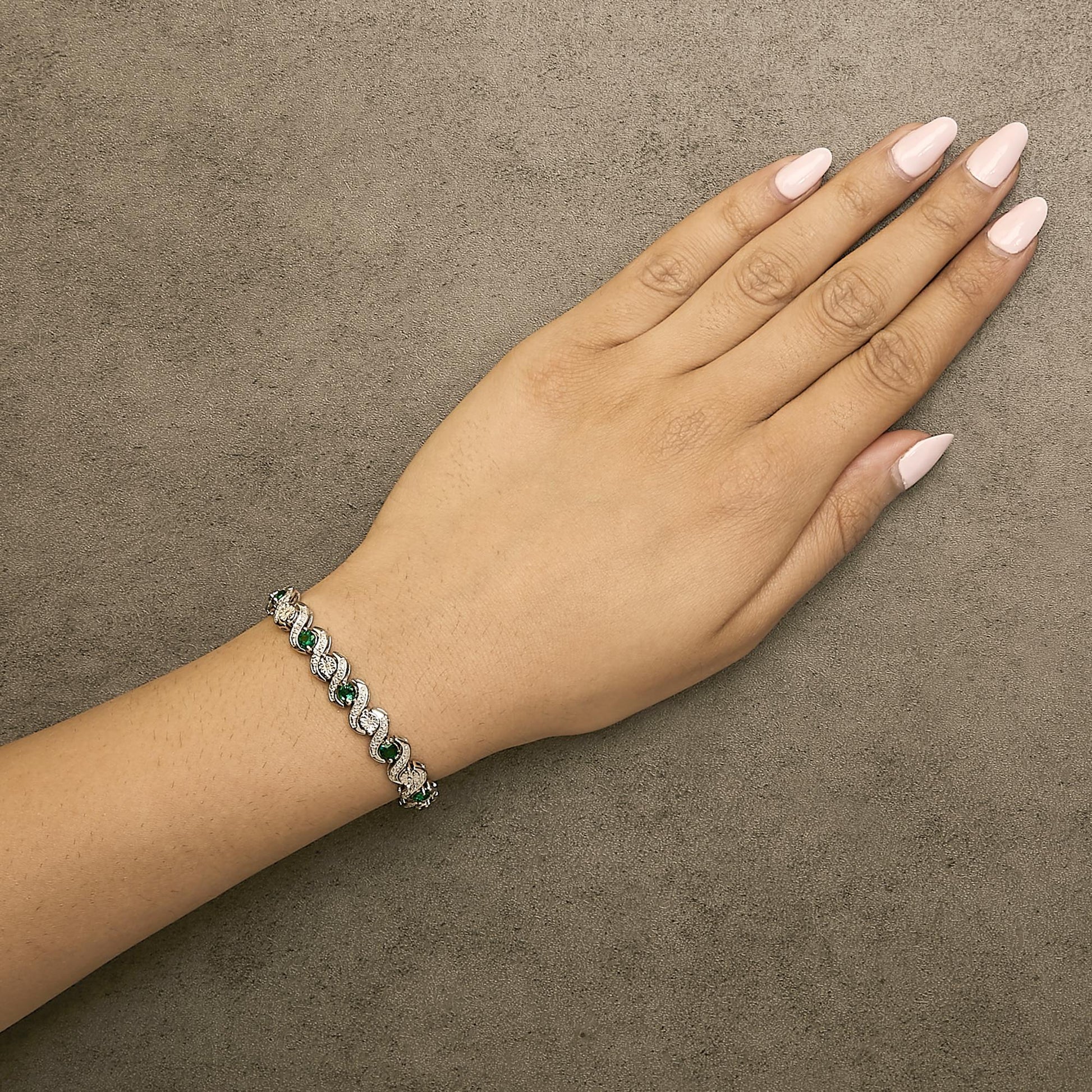 Bracelet with alternating round white and green gemstones in curved links, shown worn on a model's wrist, angled top-down.