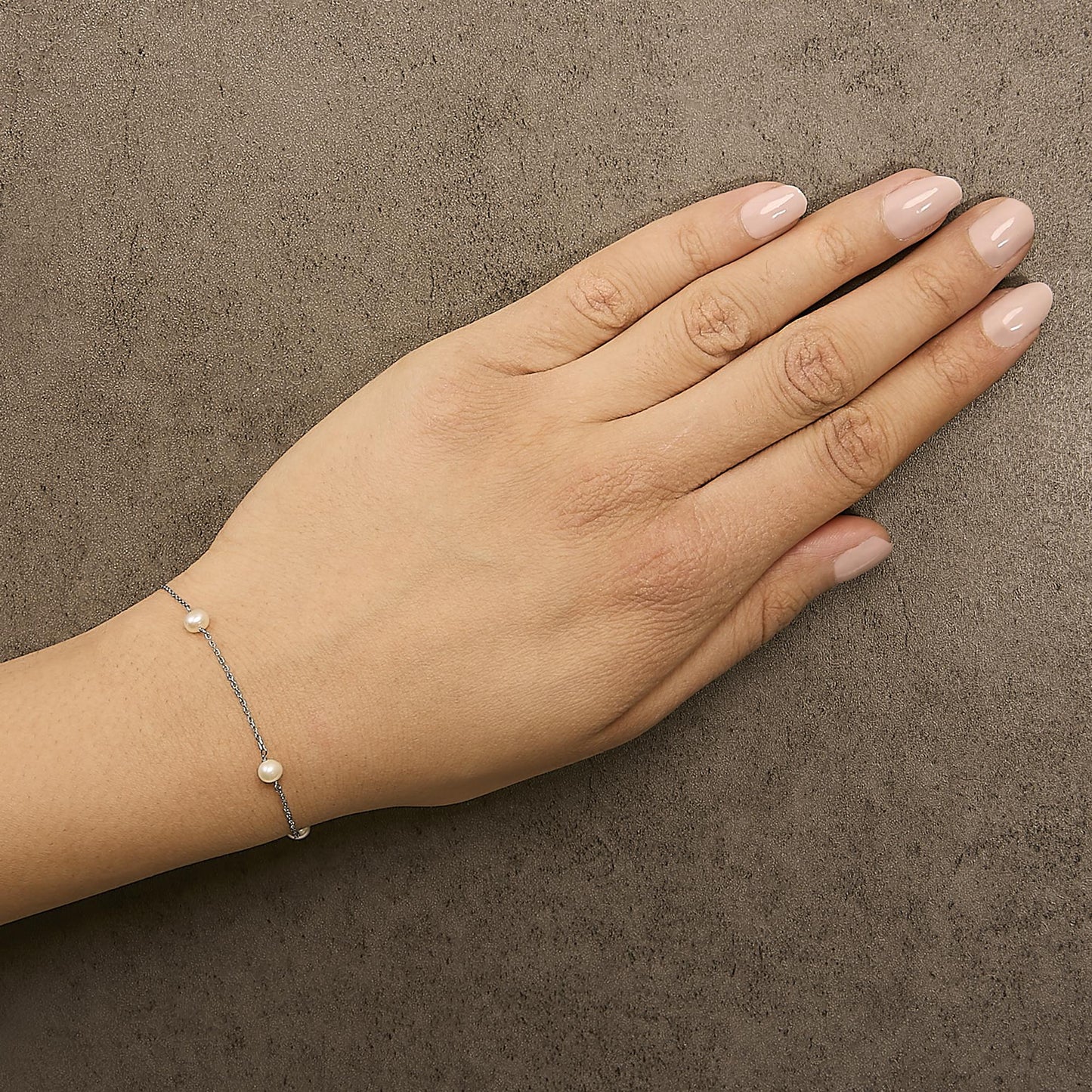 White metal delicate chain bracelet with small white gemstone beads spaced evenly, shown worn on a model's wrist, top-down angle.