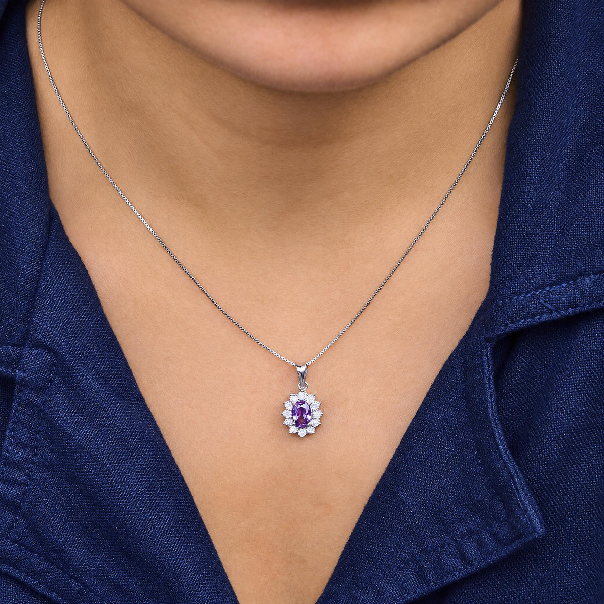 Close-up front angle of a necklace with a white metal chain and a pendant featuring an oval purple gemstone surrounded by round white gemstones, shown worn on a model.