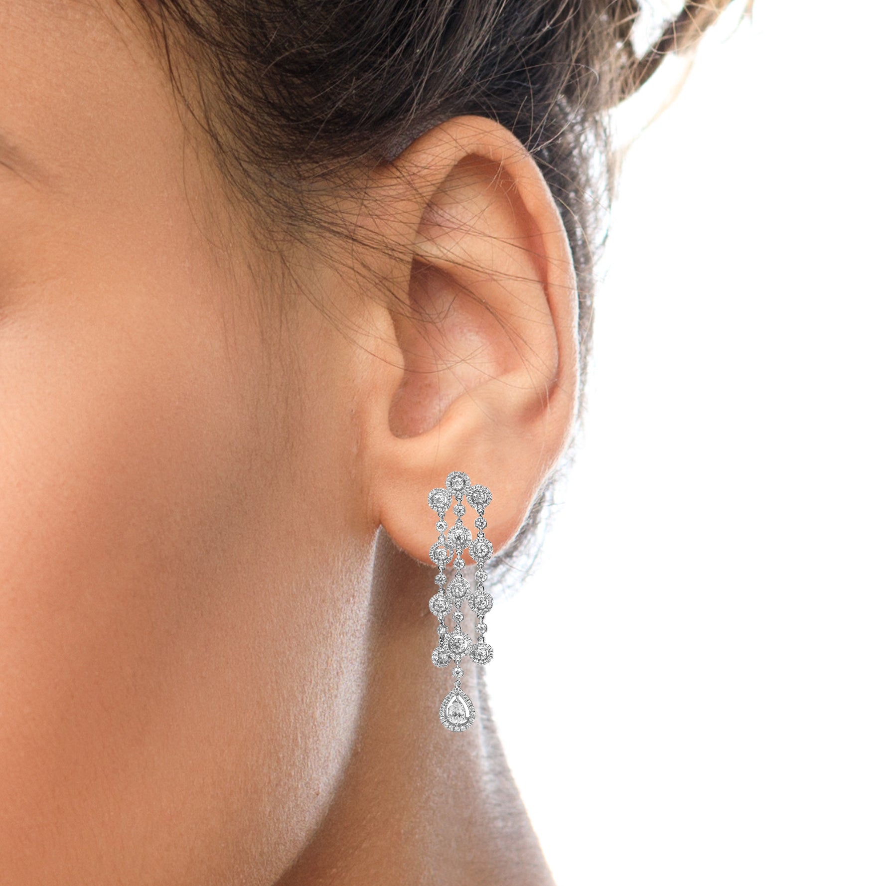 Close-up side view of a white metal earring on a model’s ear, featuring a pear-shaped gemstone drop and multiple round gemstones with prong and pavé settings in an intricate cascading design.