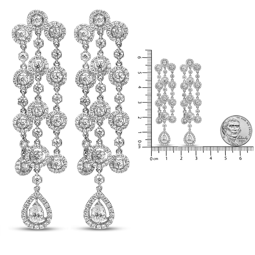 White metal dangle earrings with multiple round and pear-shaped white gemstones in prong and pave settings, shown from the front on a ruler and next to a coin for size reference.