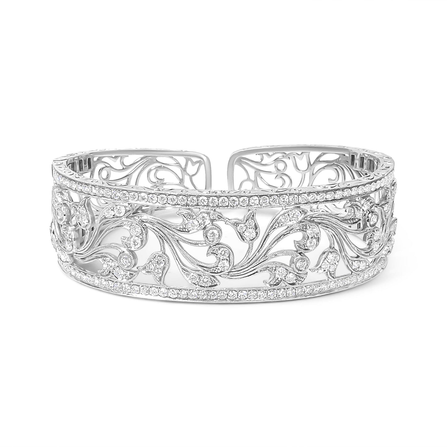 Front-facing shot of an open white metal bracelet with intricate floral scrollwork and rows of round white gemstones in pave setting along the top and bottom edges.