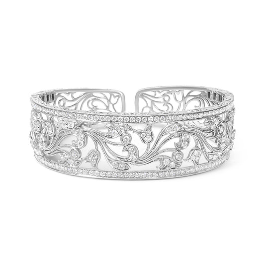 Front-facing shot of an open white metal bracelet with intricate floral scrollwork and rows of round white gemstones in pave setting along the top and bottom edges.