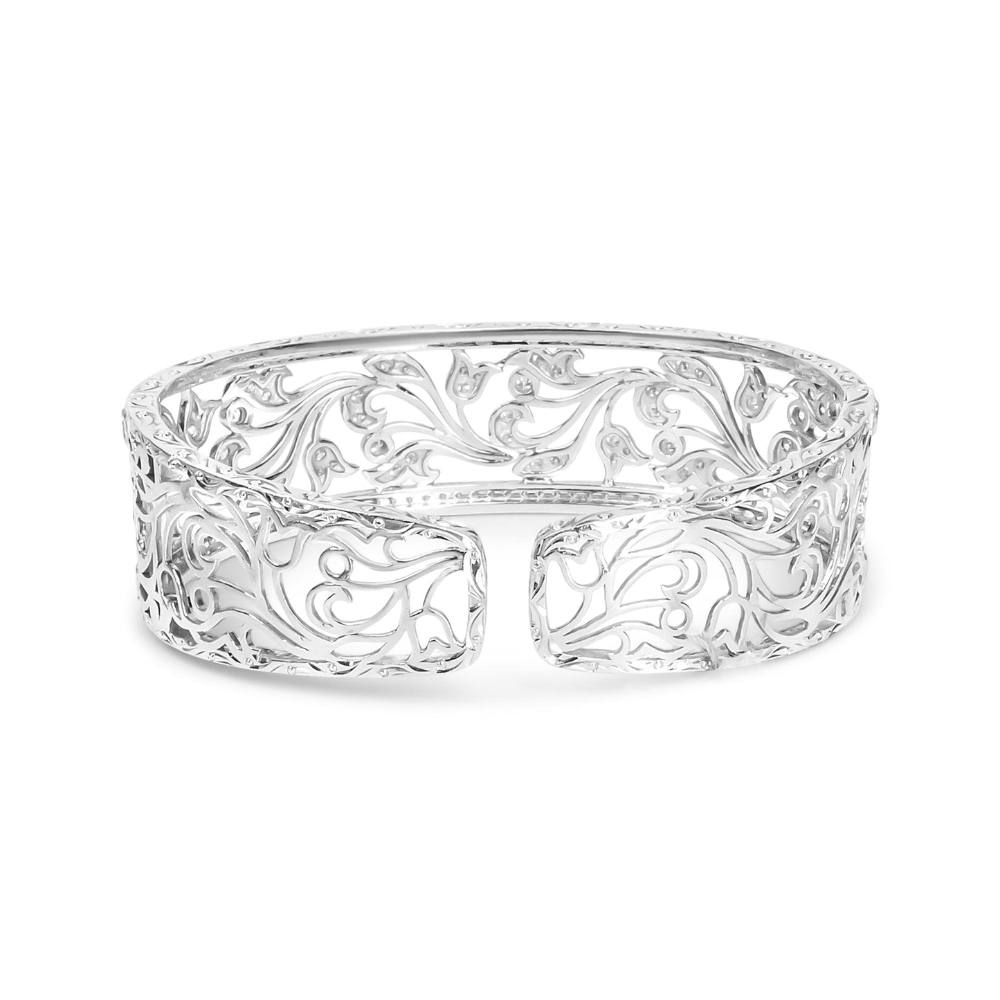 Front-facing shot of an open white metal cuff bracelet with intricate scrollwork and round white gemstones in a pave setting throughout the design.