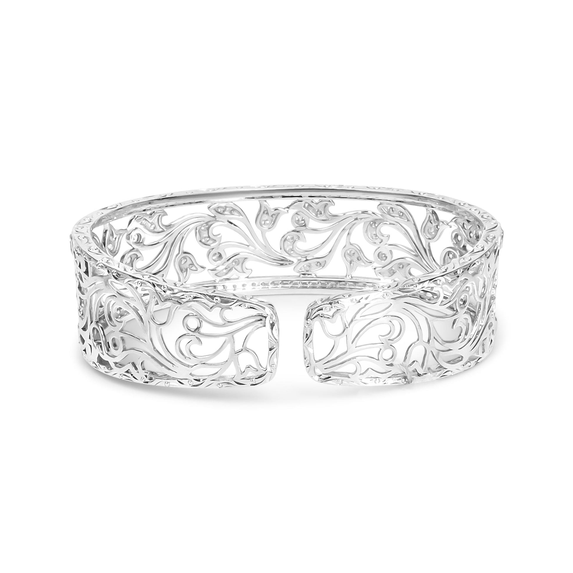 Front-facing shot of an open white metal cuff bracelet with intricate scrollwork and round white gemstones in a pave setting throughout the design.