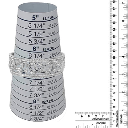 White metal bracelet with intricate openwork floral design and round white gemstones in pave setting, displayed on a size measurement cone with rulers for size reference, front-facing angle.