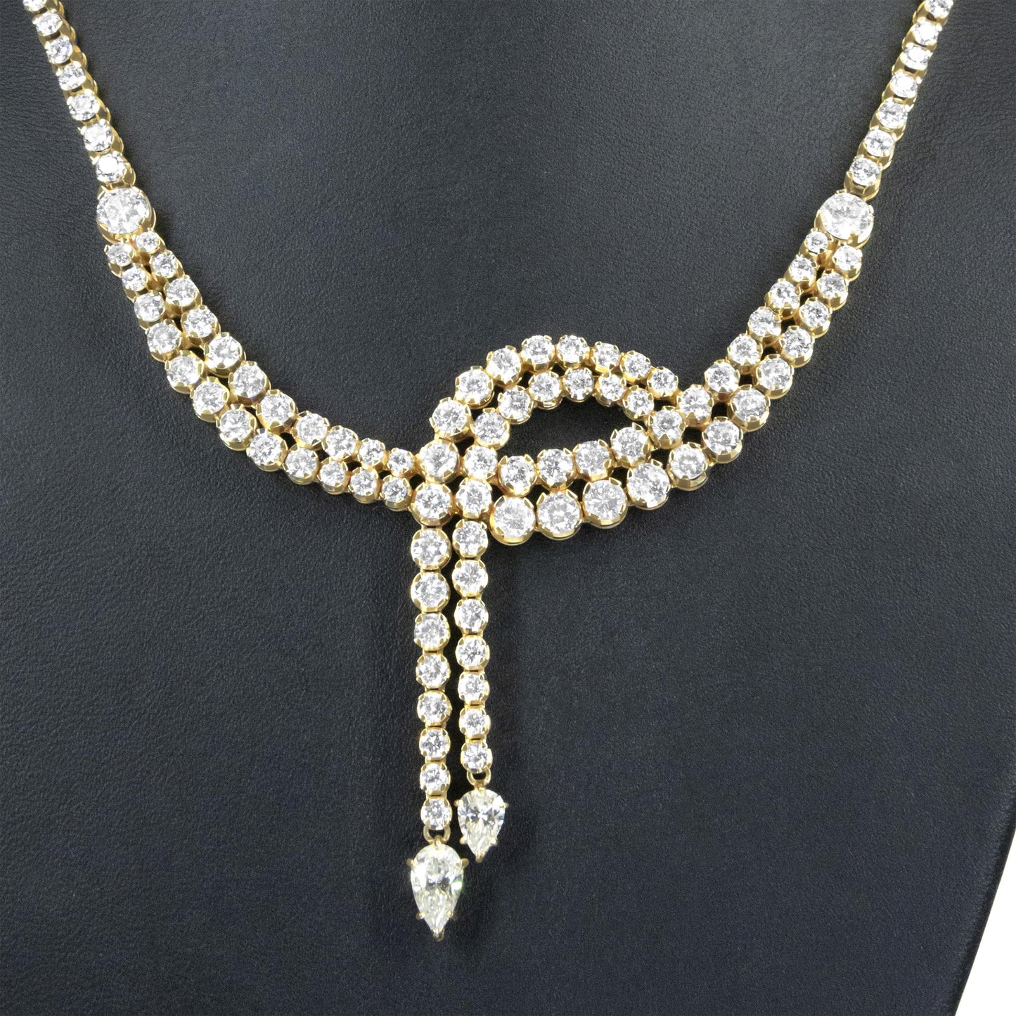 Close-up front view of a yellow metal necklace featuring multiple rows of round white gemstones in prong settings, with two pear-shaped white gemstones hanging at the center.