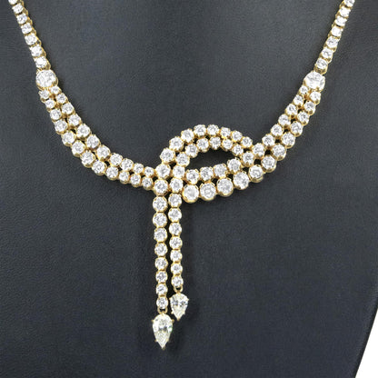 Close-up front view of a yellow metal necklace featuring multiple rows of round white gemstones in prong settings, with two pear-shaped white gemstones hanging at the center.