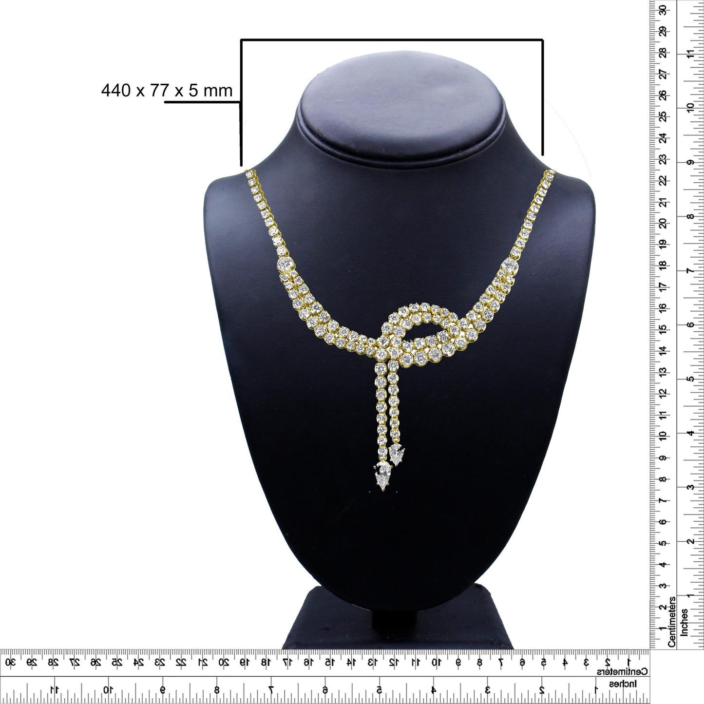 Front view of a yellow metal necklace with multiple white round and pear-shaped gemstones arranged in a looped design, displayed on a black jewelry bust with rulers on the right and bottom for size reference.