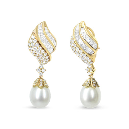 Front view of a pair of yellow metal earrings with curved designs featuring white baguette and round gemstones in channel and pave settings, each earring adorned with a large white pearl drop.