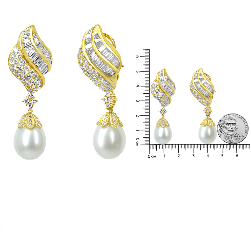 Pair of yellow metal earrings with curved design featuring white baguette-shaped gemstones in channel setting and round white gemstones in pave settings, with a single large white pearl drop, shown from the front and side angles, displayed next to a ruler and a coin for size reference.