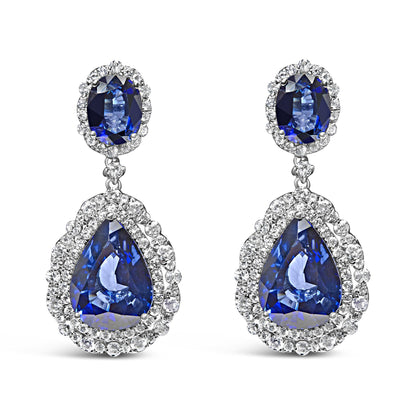 Front view of white metal drop earrings featuring oval and pear-shaped blue gemstones surrounded by white gemstones in prong settings.