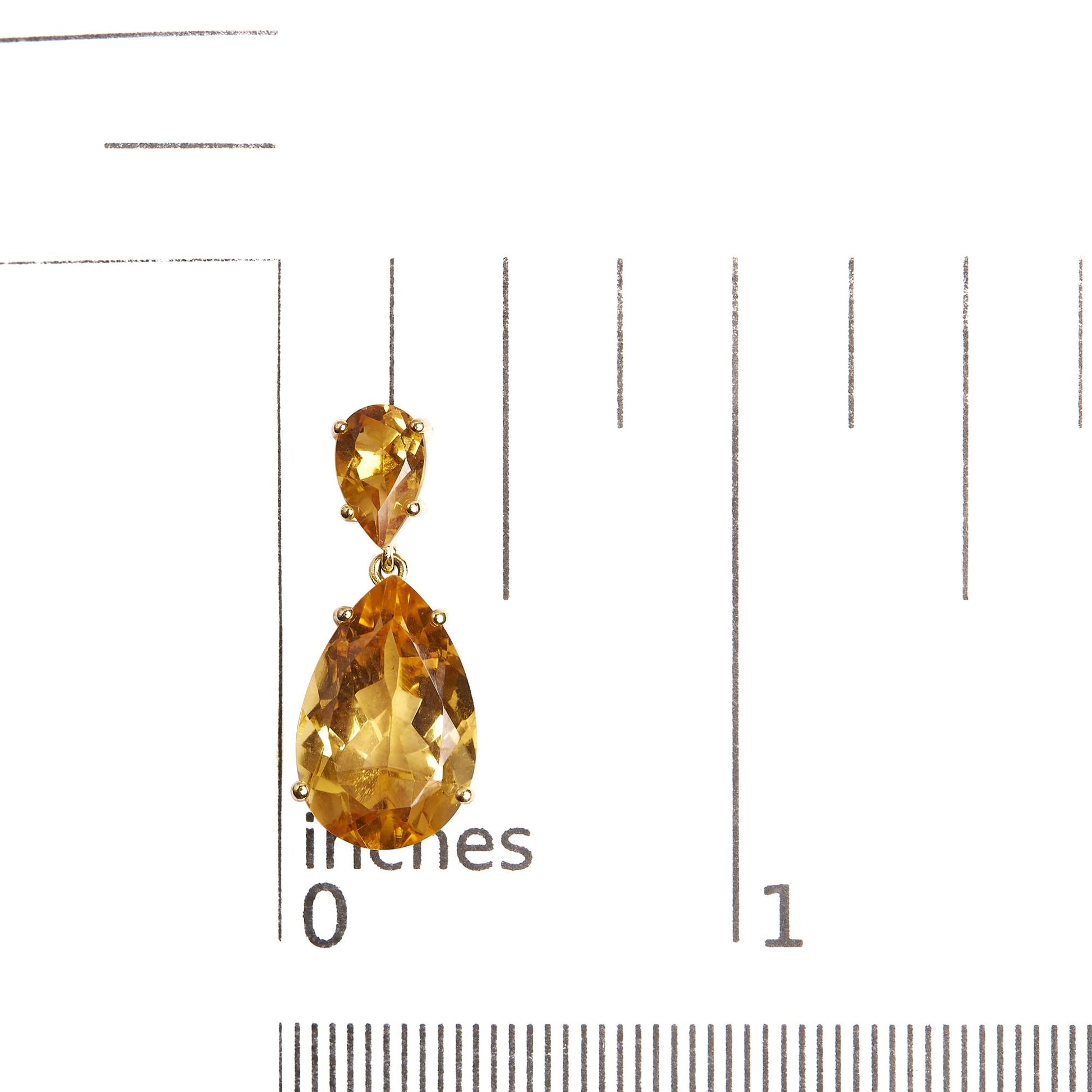 Yellow metal earring with two pear-shaped orange gemstones in a vertical drop design, shown on a ruler for size reference, front view.