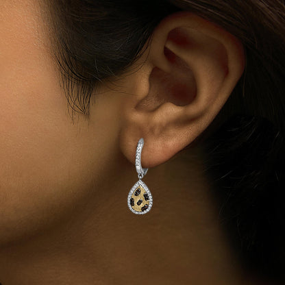 Earring with a teardrop shape featuring yellow metal and scattered orange gemstones, bordered by white gemstones, shown worn on a model's ear from a side angle.