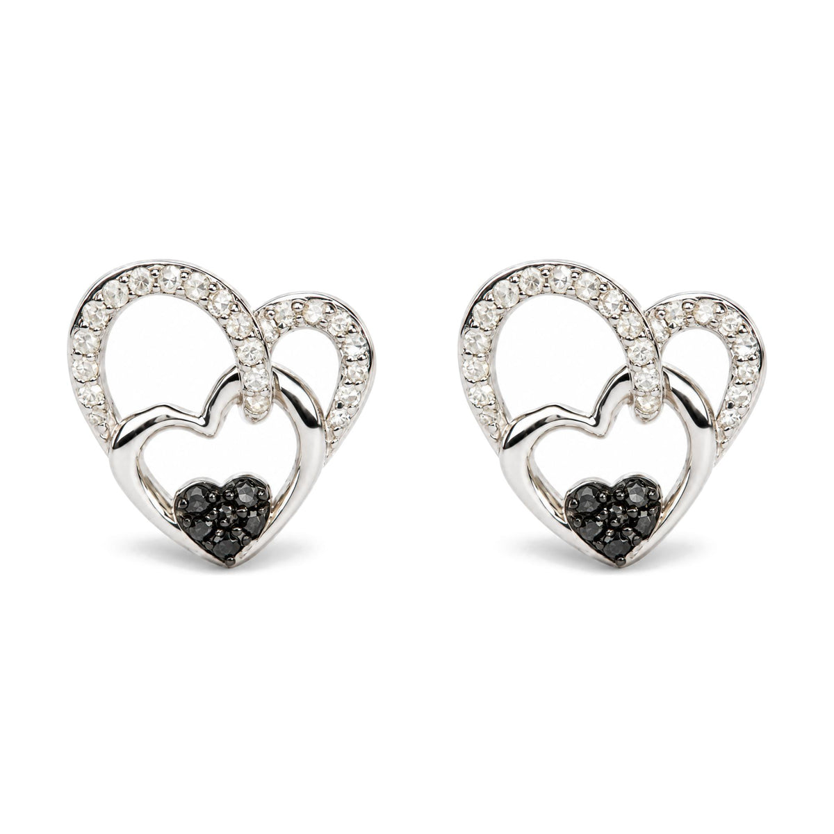 Pair of white metal heart-shaped earrings with two overlapping hearts; larger heart outlined with white gemstones and smaller heart in solid metal, accented with black gemstones at the bottom. Image shows a close-up front view of the earrings on a white background.