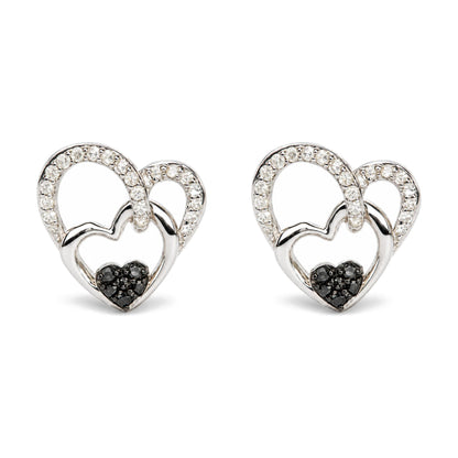 Pair of white metal heart-shaped earrings with two overlapping hearts; larger heart outlined with white gemstones and smaller heart in solid metal, accented with black gemstones at the bottom. Image shows a close-up front view of the earrings on a white background.