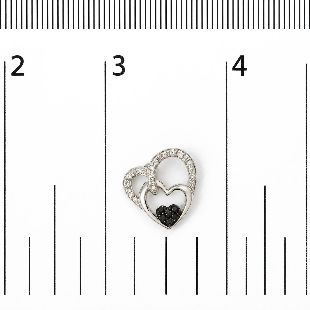Close-up front view of a pair of white metal heart-shaped earrings shown on a scale, featuring three nested hearts: the largest and middle hearts are adorned with round white gemstones in prong settings, and the smallest heart is decorated with round black gemstones in prong settings.