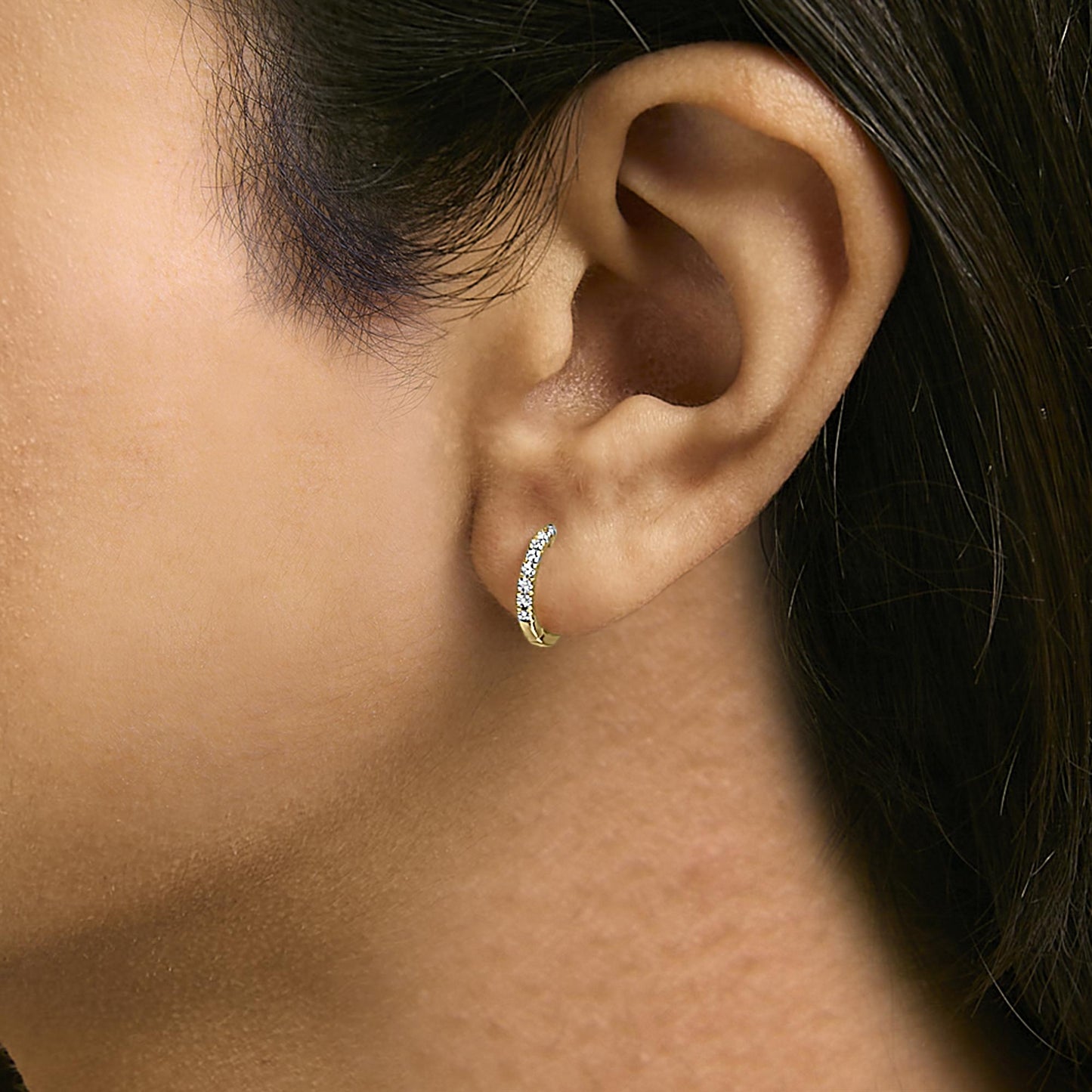Close-up side view of a model wearing a small yellow curved hoop earring set with white round gemstones in a 4-prong setting.