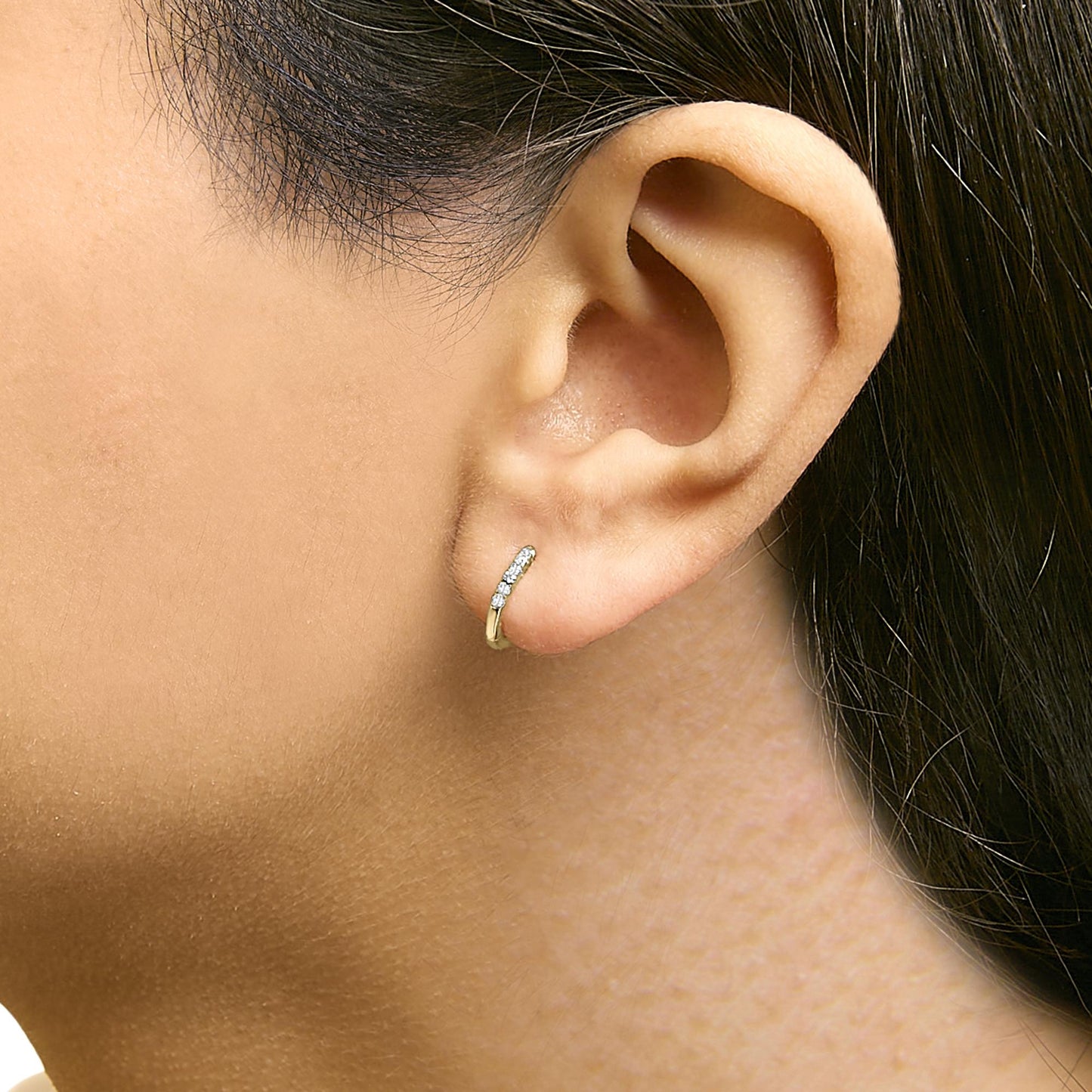 Close-up side view of a model wearing a small yellow hoop earring set with round white gemstones in shared prong settings.