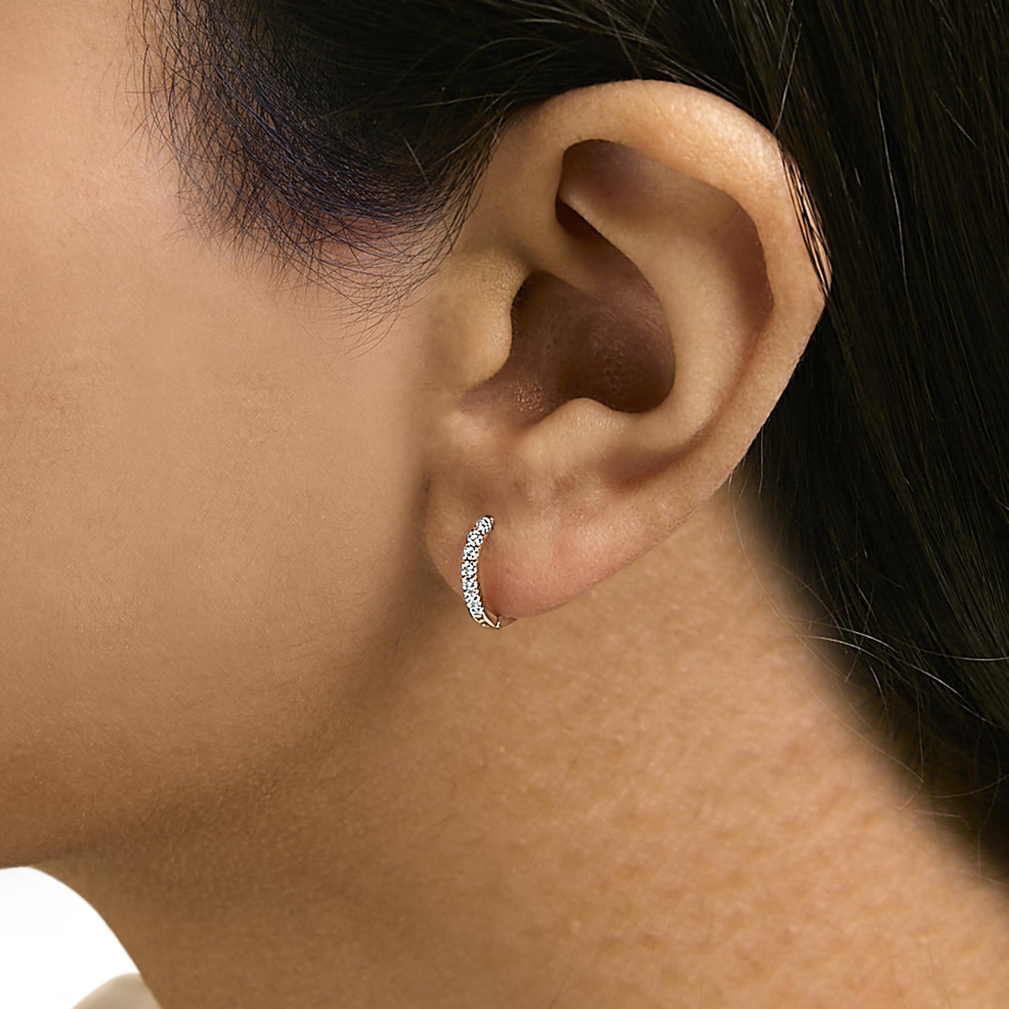 Close-up side view of a model wearing a curved rose metal earring set with multiple round white gemstones in a 4-prong setting.
