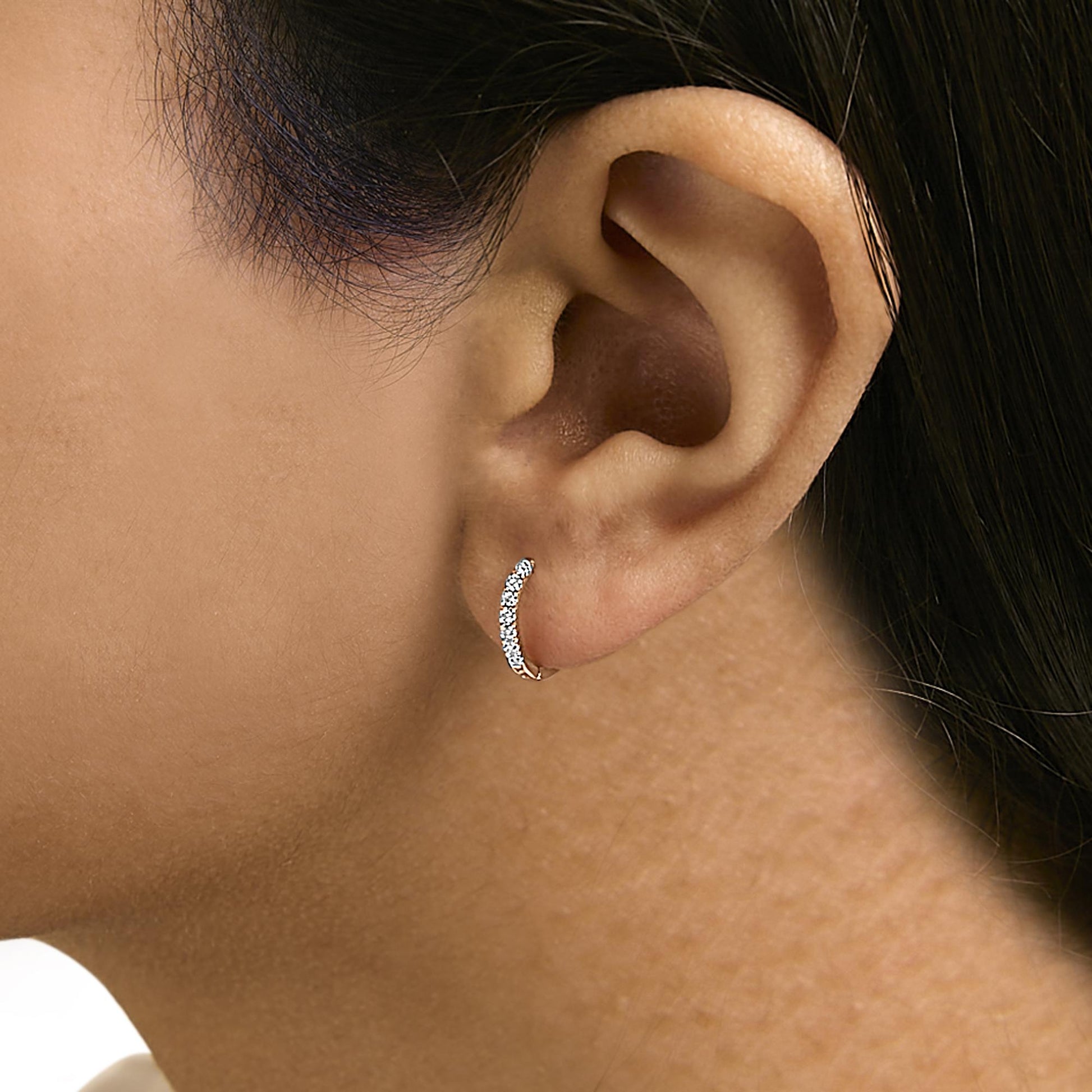 Close-up side view of a model wearing a curved rose metal earring set with multiple round white gemstones in a 4-prong setting.