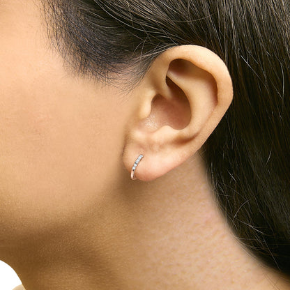 Close-up side view of a model wearing a small rose-colored hoop earring set with round white gemstones in a shared prong setting.