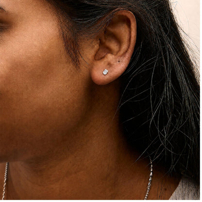 Close-up side angle of a model wearing white metal earrings with emerald-shaped white gemstones in a four-prong setting.