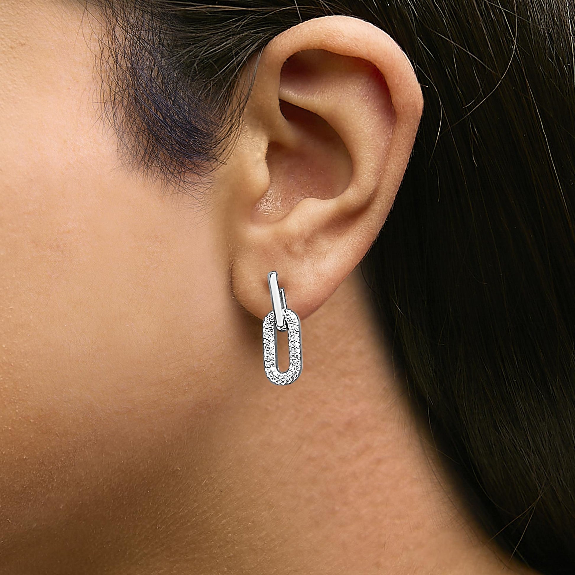Close-up front-angle view of a model wearing white metal earrings featuring a link-shaped design with round white gemstones in a shared prong setting.