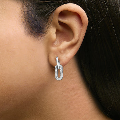Close-up front-angle view of a model wearing white metal earrings featuring a link-shaped design with round white gemstones in a shared prong setting.