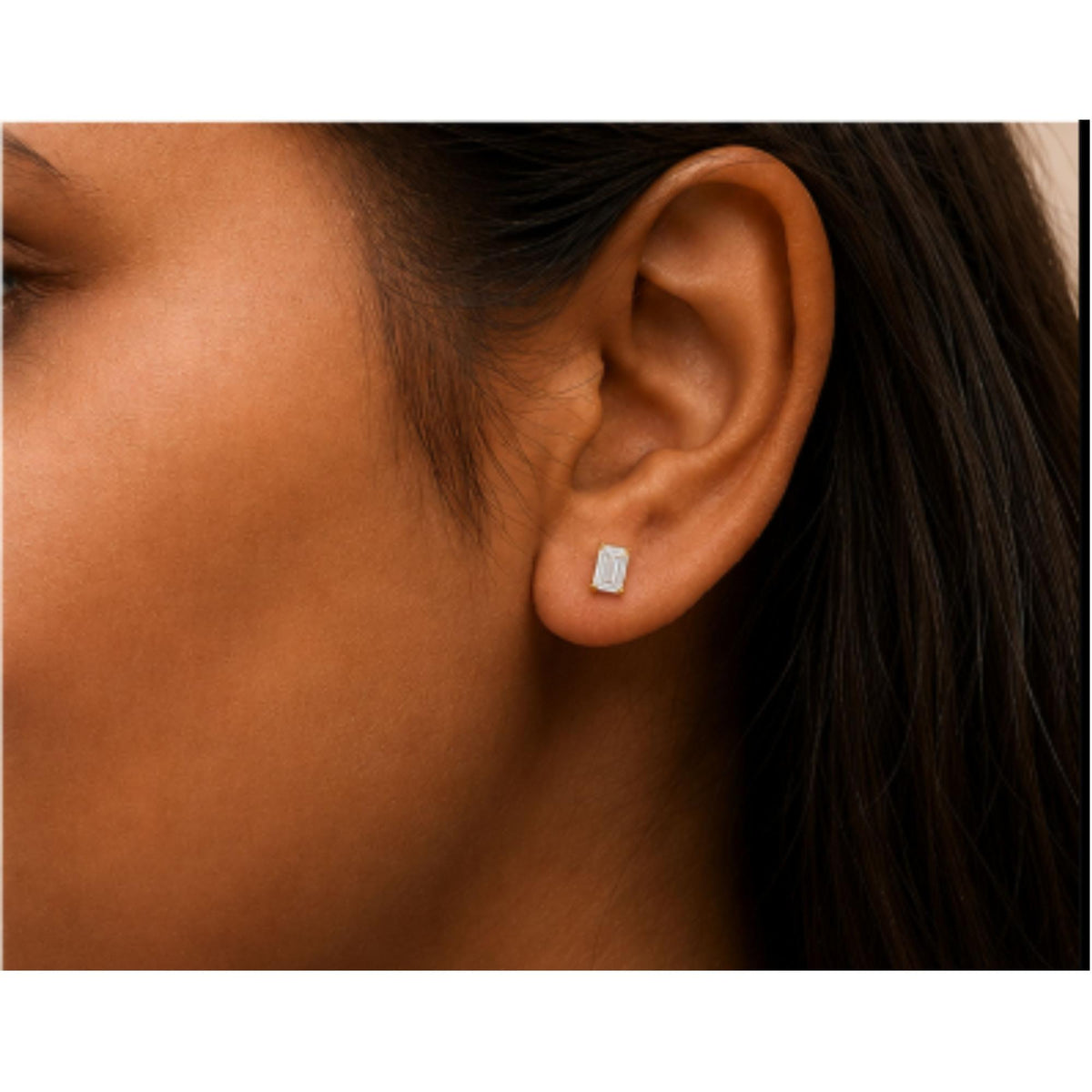Close-up side view of a model wearing a yellow metal earring with a white emerald-shaped gemstone in a four-prong setting.