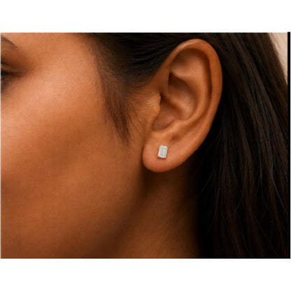 Close-up side view of a model wearing a yellow metal earring with a white emerald-shaped gemstone in a four-prong setting.