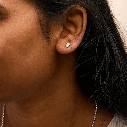 Close-up side angle of a model wearing a white metal earring featuring an emerald-shaped white gemstone with a 4-prong setting.