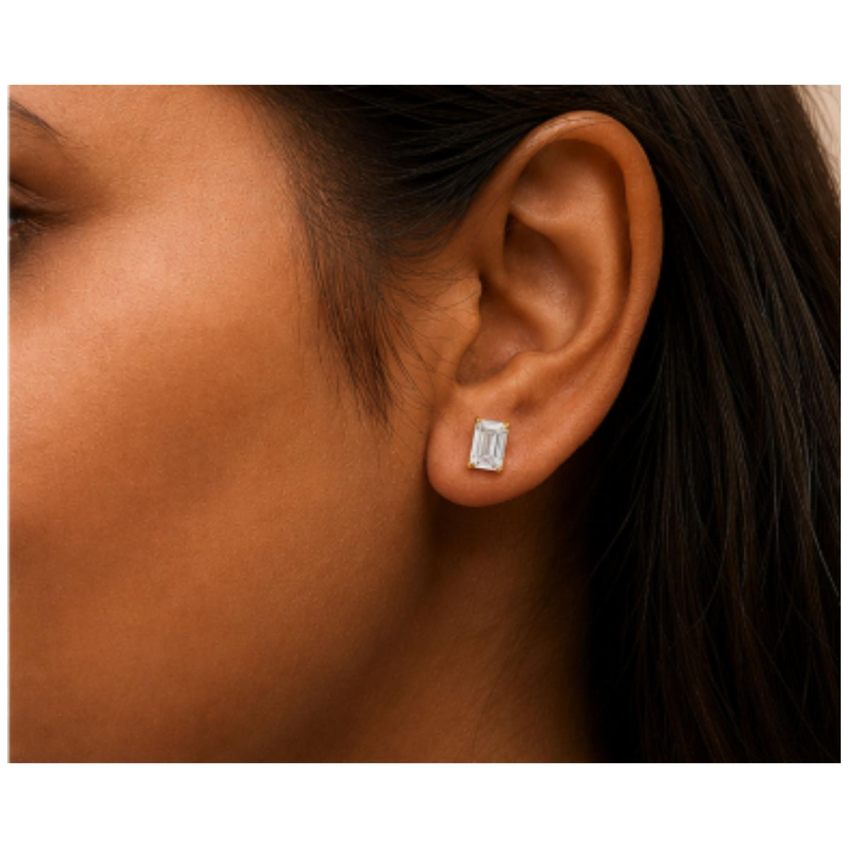 Close-up side view of a model wearing a yellow metal earring with a white emerald-shaped gemstone in a four-prong setting.